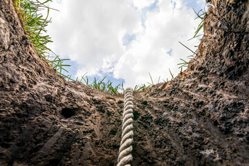 Looking up from hole in ground with rope. Lifeline, debt, mental health help concept.  - obrazy, fototapety, plakaty