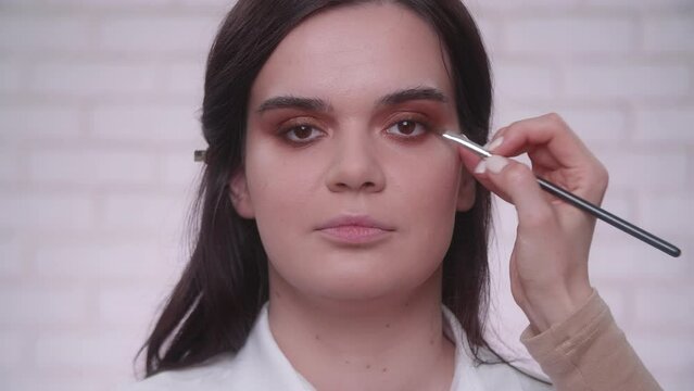 Young caucasian woman prepares for a photo session, while applying make-up. Professional makeup artist doing smoky eyes effect with liner and eye shadow. High quality 4k footage