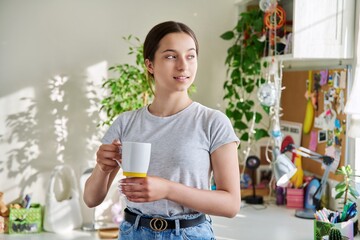 Teenage girl 14, 15 years old holding mug, standing at home