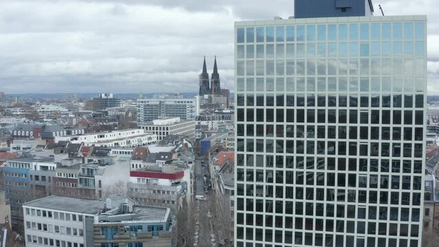 Descending shot along modern high rise office building with large glossy windows reflecting sky and building in urban neighbourhood. Cologne, Germany