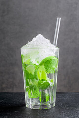 Fresh mojito made of citrus fruit and green mint leaves on dark background. Glass with delicious non-alcoholic beverage with crushed ice and straw on black table closeup