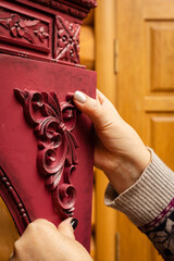 Female hands gluing new carved nice ornaments to wooden cardboard of bright red color in workshop...