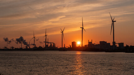 Obraz premium Silhouette of wind turbines in industrial area by the sea on sunset