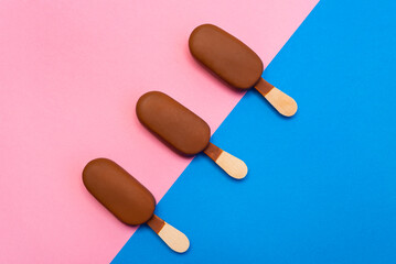 Three chocolate glazed ice cream bars on pink and blue color background