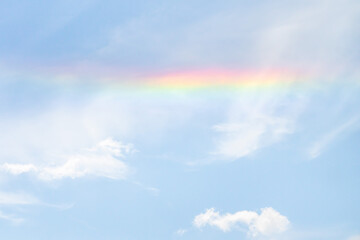 Beautiful sky background photograph of a partial rainbow reflecting on the white clouds in the sky on a sunny day.