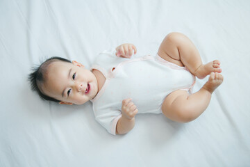 Obraz na płótnie Canvas Cute little asian baby lying on white bed with soft blanket indoors