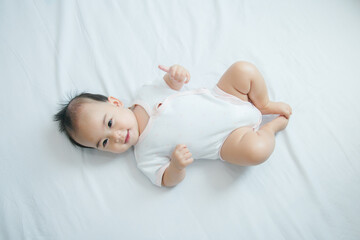 Cute little asian baby lying on white bed with soft blanket indoors