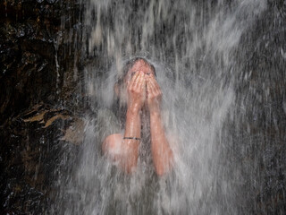 Fototapeta na wymiar White Woman Covering her Eyes from the Water Falling in the Small Waterfall in the Forest