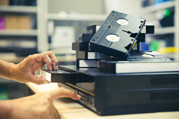 Close-up hand chooses and put or insert video cassette tape VHS on video record playback concept of retro style or vintage electric and electronic appliances multimedia player device old fashioned.