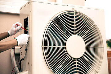 Technician Air conditioning repairman using measuring equipment checking electrical at circuit breaker on outdoor air compressor after install and check refrigerant system maintenance.