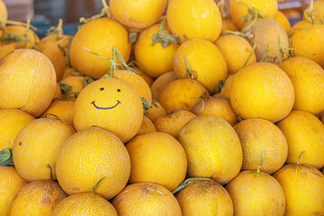 Many organic ripe melons at the farmers seasonal market. Smile is drawn on one fruit