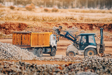 a tractor loads bricks and other construction debris with a bucket into a truck on a excavation site
