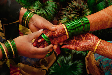 At a pre wedding ceremony a lady bangle seller is putting green glass bangles on the henna...