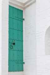 Closed turquoise metal door with an old lock in a white brick house. Historical architecture. Vertical.