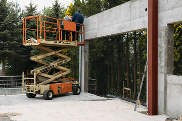 Scissor Lift Platform with workers on a construction site. Building concreate house with mobile...