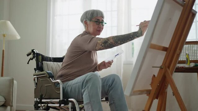 old senior asian female tattoo using art therapy while his legs is injured at home,asian elder woman spend recovering of her leg is getting better with painting canvas art in living room at home
