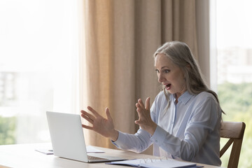 Older businesswoman open mouth gawp at laptop get unbelievable commercial offer feels shocked look...