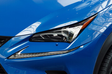 Close-up headlights of a modern blue color car. Detail on the front light of a car. Modern and expensive car concept. The car is in the showroom. Automotive concept. Classic blue color. LED light