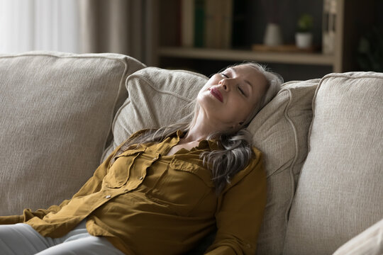 Peaceful middle-aged woman sleeping leaned on soft cushions looks without energy after fruitful day, relax alone on cozy sofa, take healthy daytime nap. Fatigue relief, rest, conditioned air concept