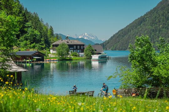 Ostufer or south bank at weissensee austria, beautiful alpine lake with visible village and boat transport. Cyclists and tourists also visible.