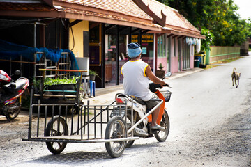 Fototapeta na wymiar Thai people riding biking motorcycle and pull trolley cart on small street go to highway road in Wat Tenplai temple of Si Prachan district of Suphanburi city on May 27, 2022 in Suphan Buri, Thailand