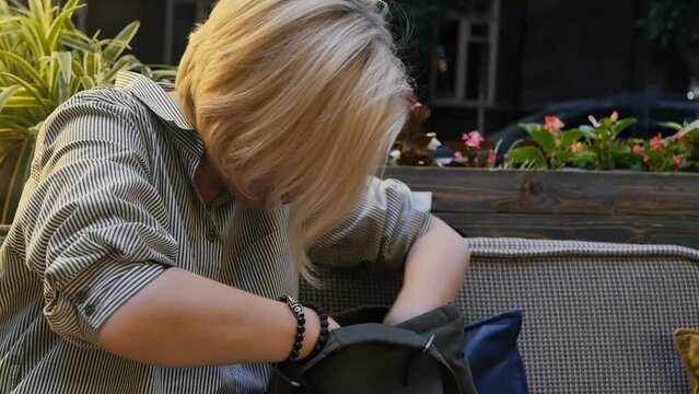 an adult Caucasian attractive blonde rummages hastily and frightened in her bag looking for some object. A woman frantically looking for something in her bag leaving an important thing somewhere