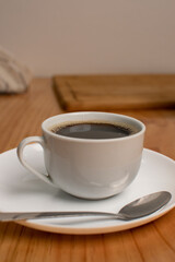 A white cup of black coffee with a spoon in a wood table