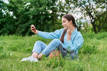 Teenage female student sitting on the grass using smartphone.