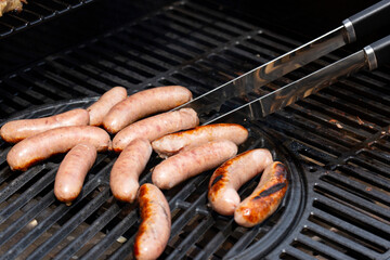 Pork sausages being turned with tongs on a gas barbecue.  Outdoor cooking concept