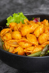 Pasta with a sun dried tomato sauce with lettuce in a black bowl. On a black stone background