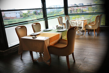 A restaurant consisting of brown wooden chairs and a table with a white fabric cover. Empty catering plates and forks, spoons, knives on a white tablecloth.	
