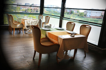 A restaurant consisting of brown wooden chairs and a table with a white fabric cover. Empty catering plates and forks, spoons, knives on a white tablecloth.	

