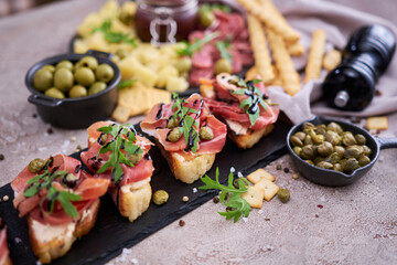 bruschetta with prosciutto ham and capers with traditional antipasto meat plate on background