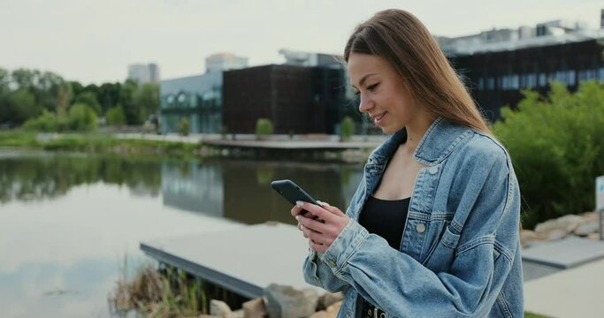 Portrait of a beautiful woman in casual clothes and using smartphone on the street. Female using phone online, messaging and browsing internet.