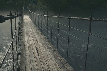 old wooden long suspension bridge over the Belaya mountain river, in nature, thick mystical fog over the water at night in the moonlight