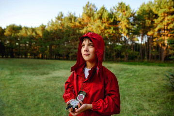 A boy in a red windbreaker against the backdrop of a forest with a compass in his hand.