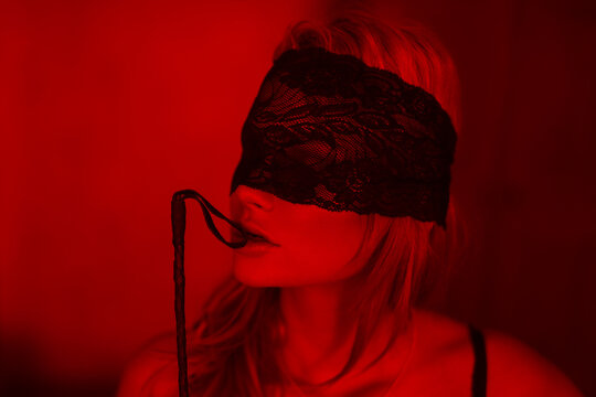 Sexy woman in lace eye cover bite whip in red light