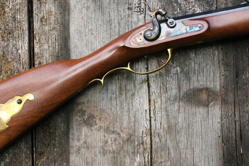 A close-up of the percussion lock and the stock of a Kentucky rifle on an old plank background