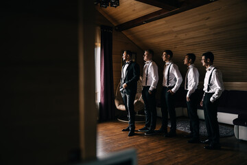 strictly dressed groom and friends look out the window in anticipation of the bride and bridesmaids.