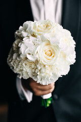 A beautiful wedding bouquet of spray and peony roses in the hands of the groom.