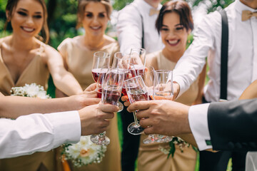 newlyweds with friends stand together and hold crystal glasses, laughing, celebrate wedding day.