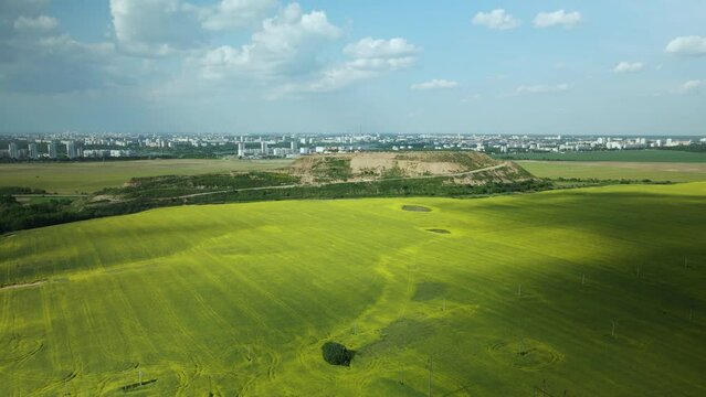 Blooming rapeseed field. On the edge of the field there is a pond. A mothballed city dump is visible on the horizon. Aerial photography.