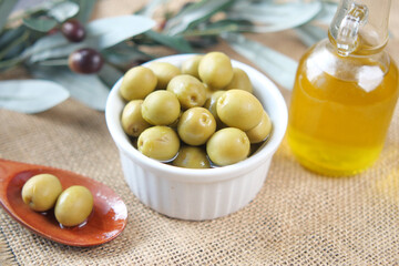 bottle of olive oil and fresh olive in a container on table .