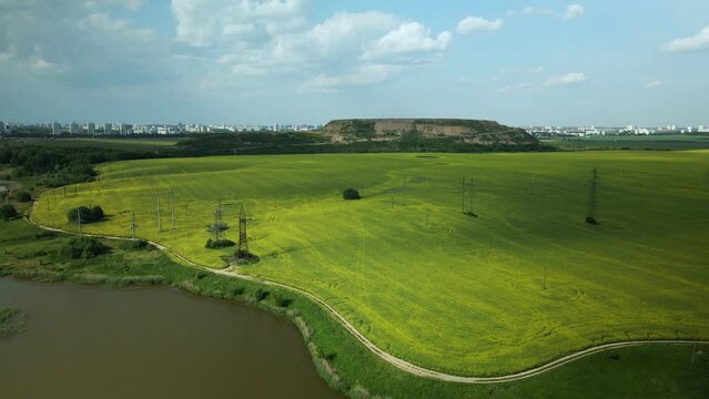 Blooming rapeseed field. On the edge of the field there is a pond. A mothballed city dump is visible on the horizon. Aerial photography.
