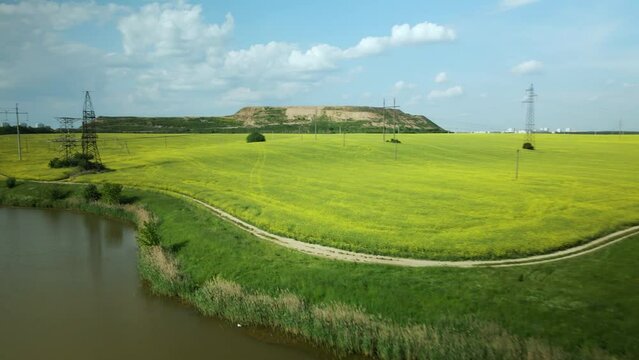 Blooming rapeseed field. On the edge of the field there is a pond. A mothballed city dump is visible on the horizon. Aerial photography.