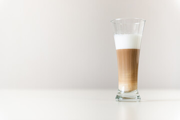 multi-layered coffee in a transparent glass on a gray background and a white table