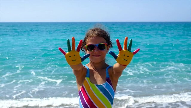A child at the sea with paints on her hands a smile. Selective focus.