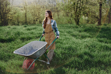 A happy woman with a cart works in her country home in the countryside against a backdrop of green...