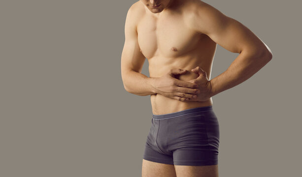 Young muscular man experiencing liver pain standing near copy space on gray banner background. Cropped image of man with naked torso with hepatitis, rubs his right side. Concept of liver disease.