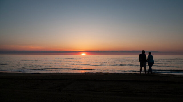 Two people, man and woman, watch the sunrise at the ocean © Tamara Harding